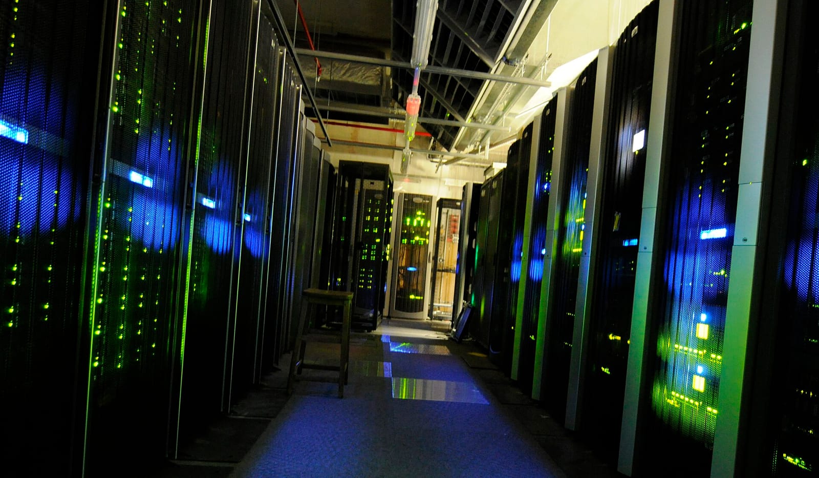 A server room aisle at night, rack lights glowing green and blue